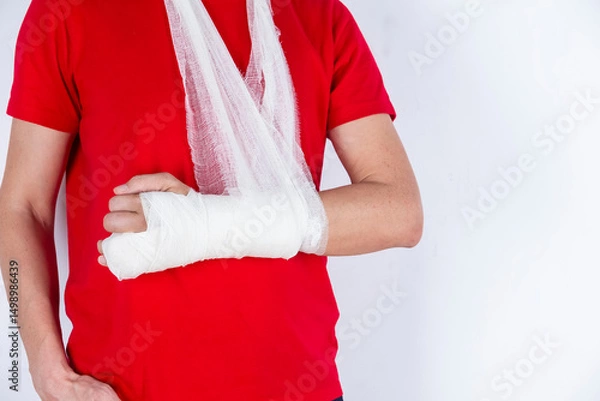 Fototapeta Medical Concepts. Closeup of Body Parts of Caucasian Man in Red Shirt with Broken Hand In Plaster and Bandaid Isolated on White Background.