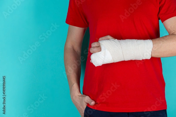 Fototapeta Medical Ideas and Concepts. Closeup of Caucasian Man Damaged Broken Hand In Plaster and Bandaid Isolated on Turquoise Background.