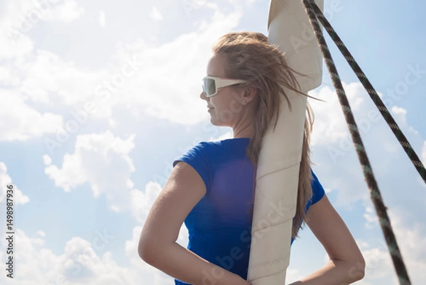 Fototapeta Sea Travel Concepts. One Winsome Happy and Smiling Positive Caucasian Sailor Woman Standing Near Mast On Deck Relaxing on White Yacht At Daytime on Board.