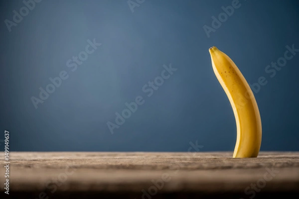 Obraz Single banana standing upright on wooden table with blue background