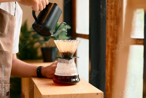 Fototapeta Close up of man brewing coffee with pour over method using a glass dripper in a kitchen