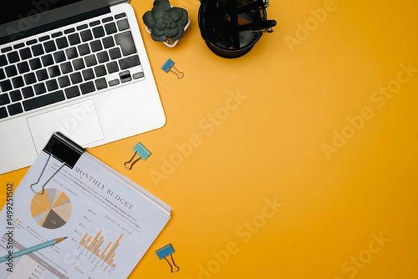 Fototapeta Modern office desk with laptop, monthly budget report, stationery, and succulent on yellow background