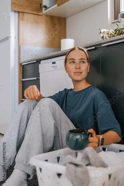 Obraz Young woman drying laundry on balcony during slow morning at home. Real moment, Gen Z lifestyle, sustainability, calm domestic routine, mindful living, eco-conscious habits, natural light.