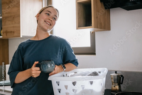 Obraz Young woman drying laundry on balcony during slow morning at home. Real moment, Gen Z lifestyle, sustainability, calm domestic routine, mindful living, eco-conscious habits, natural light.