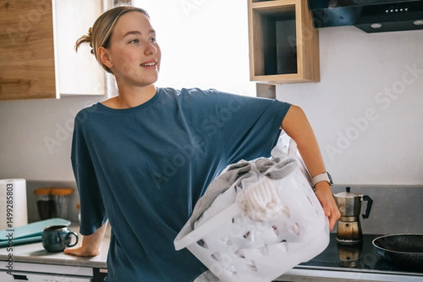 Obraz Young woman drying laundry on balcony during slow morning at home. Real moment, Gen Z lifestyle, sustainability, calm domestic routine, mindful living, eco-conscious habits, natural light.