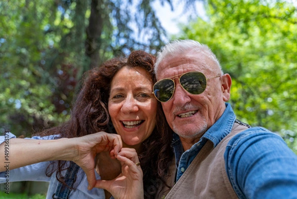 Obraz beautiful middle aged couple taking selfie showing heart symbol with hand outdoors