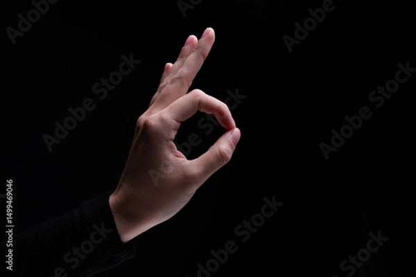Obraz Female hand showing the ok gesture on a black background. Okey hand sign