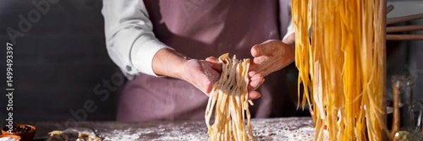 Obraz Caucasian female hands holding raw fettuccine noodles after drying