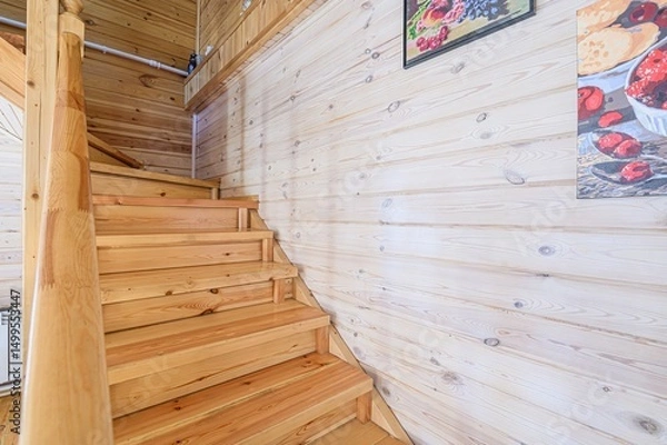 Fototapeta Wooden staircase with handrail against a light wood paneled wall. Artwork hangs on the wall.
