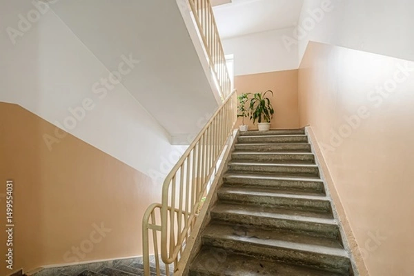 Fototapeta staircase with beige walls, white accents, a light yellow railing, and plants on the landing.