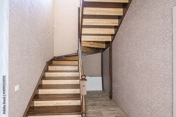 Fototapeta wooden staircase with brown-stained treads and light wood risers leads upwards. The walls are textured.