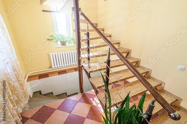 Fototapeta spiral staircase with wooden steps ascends in a room with yellow walls. A plant and radiator are visible near the bottom