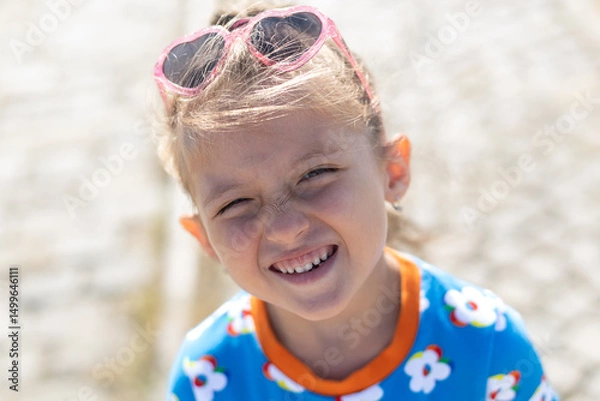 Fototapeta Happy little girl with long brown hair wearing a princess headband winking and smiling at the camera. Outdoor close-up portrait with soft natural light and a blurred background...