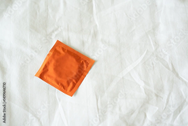 Obraz Unused condom lying on a rinkled white bedsheet.