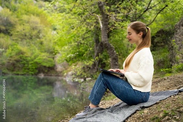 Fototapeta Full body side view of young woman in casual looking at laptop pc computer screen distance learn remote work rest relax in daylight sit near lake, freelance lifestyle, digital nomad outdoors in nature