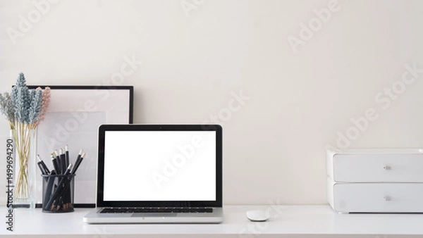 Fototapeta Simple home office with blank photo frame, stationery  and laptop with blank screen for displaying mockups.