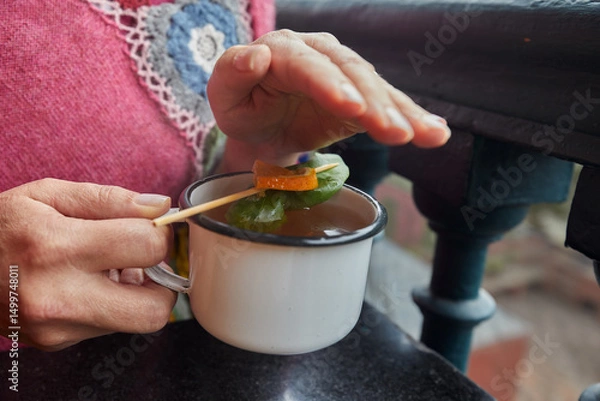 Fototapeta A comforting herbal tea infused with coca leaves and citrus peel, traditionally used in the Andes to relieve cold symptoms. Served warm in a rustic enamel mug, this natural remedy offers warmth.