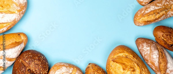 Fototapeta Different types of bread loaves arranged on a light blue surface, creating a frame with empty space in the center