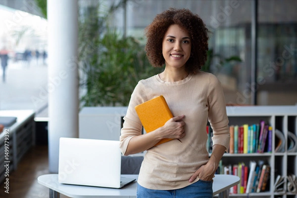Fototapeta Attractive young female university student using a laptop while studying in the library, modern education