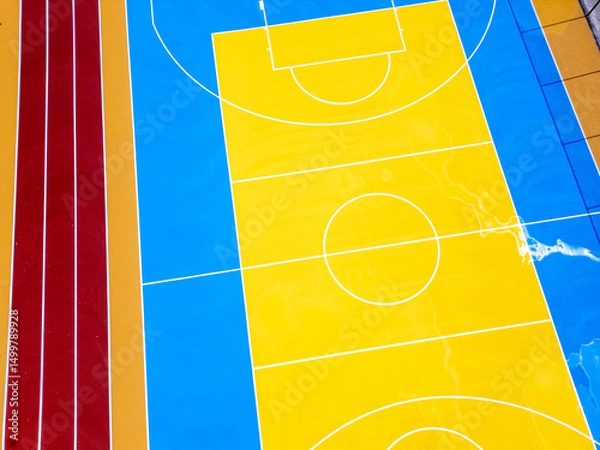 Fototapeta Aerial view of a colorful outdoor basketball court with vibrant blue and yellow markings, two hoops, and symmetrical layout. Shot from directly above.