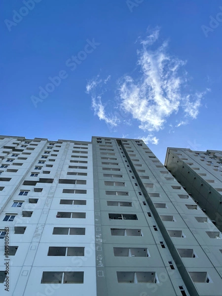 Fototapeta High-rise building with windows on the sides with a bright blue sky background. low angle photo of a high-rise building