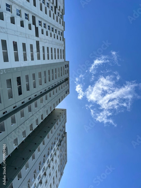 Fototapeta High-rise building with windows on the sides with a bright blue sky background. low angle photo of a high-rise building