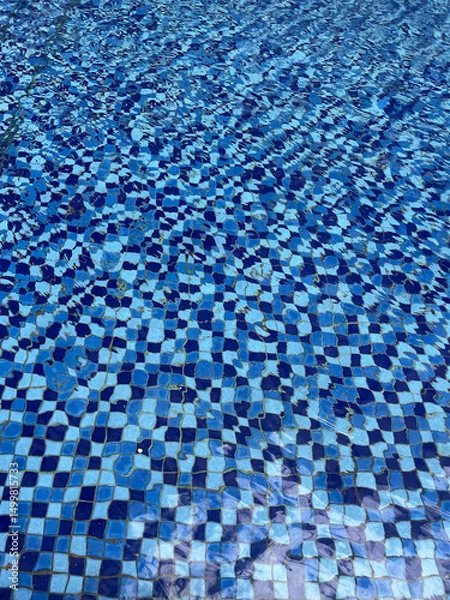 Fototapeta Pool floor background with gently wavy water and small checkered pattern ceramic mosaic floor in blue
