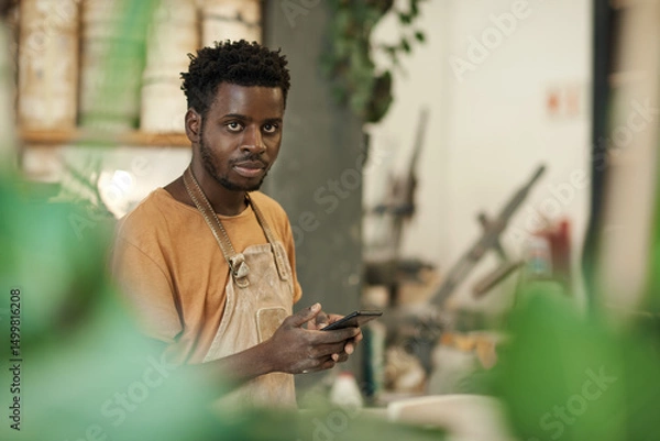 Fototapeta African ceramist using a phone while working in a pottery studio