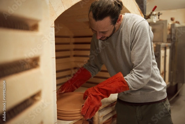 Fototapeta Ceramist taking plates from a workshop kiln after firing