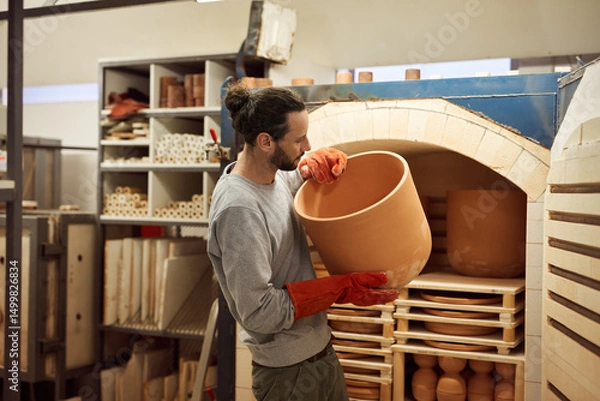 Fototapeta Ceramist removing a large clay pot from a workshop kiln