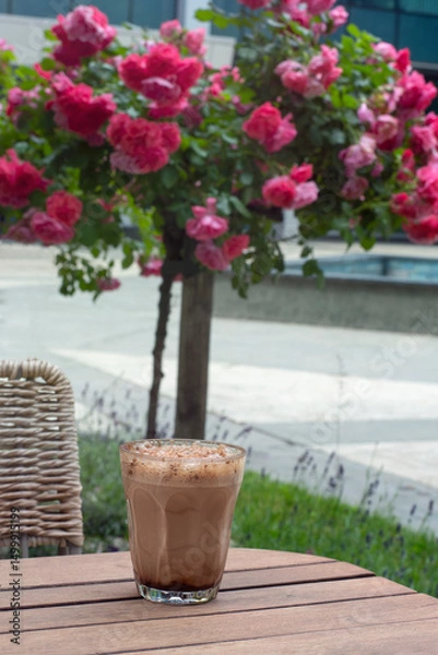 Obraz Mocha coffee in a glass on a café patio table by a rose bush
