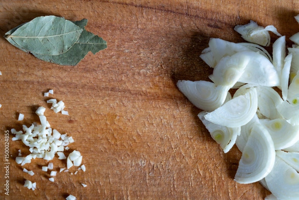 Fototapeta Chopped onions and bay leaves on a wooden cutting board