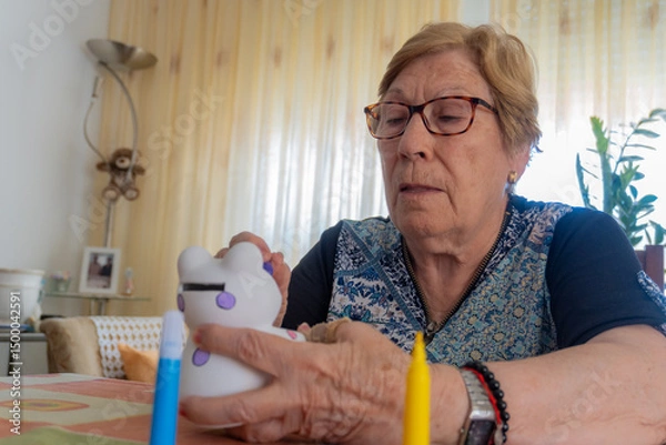 Obraz An elderly woman with Alzheimer's has fun painting a figurine at home.