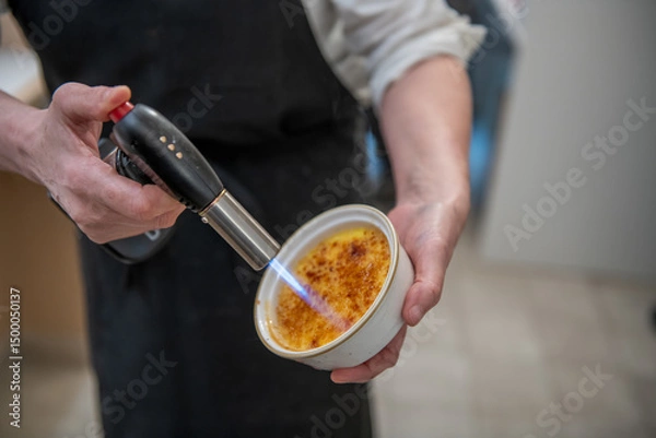 Fototapeta Chef preparing creme brulee with torch flame in elegant kitchen setting