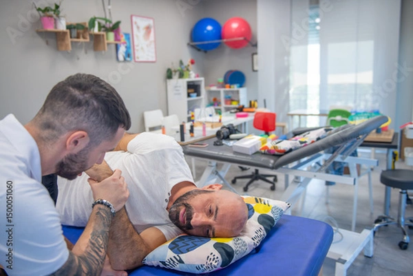 Fototapeta Osteopath practising physiotherapy on a couch to a man's shoulder