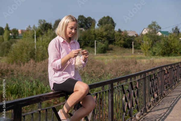 Obraz A happy smiling young woman knits on the street. Knitting Day in public