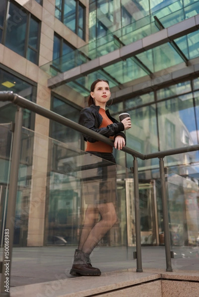Fototapeta Girl with hot coffee against the background of a modern city building.