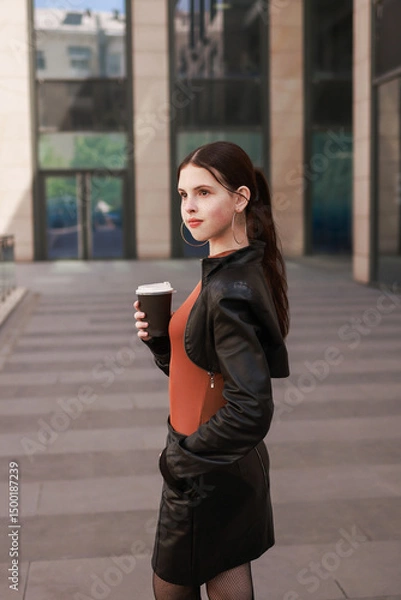 Fototapeta Girl with hot coffee against the background of a modern city building.