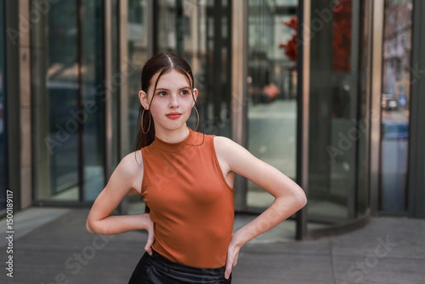 Fototapeta A girl with freckles in a leather skirt near a skyscraper.