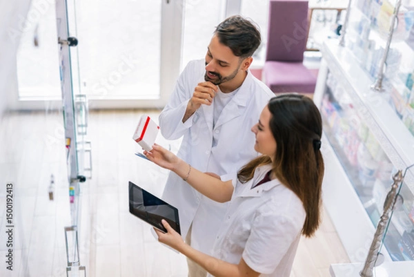 Fototapeta Pharmacists Selecting Medicine from Shelf Using Tablet in Pharmacy