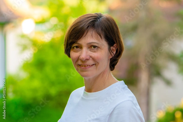 Fototapeta A 50-55 year old woman against a green backdrop, smiling at the camera.
