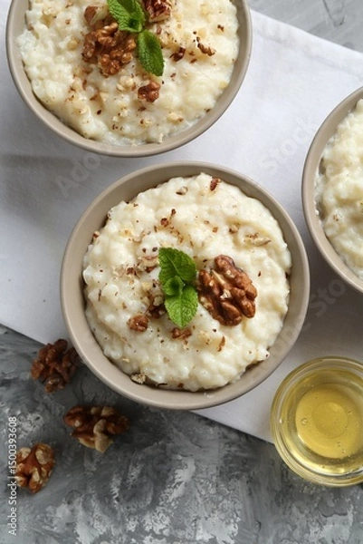 Obraz Delicious rice pudding with walnuts, mint and honey on grey table, flat lay