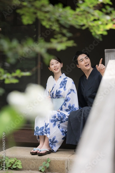 Fototapeta 夫婦やカップルでの浴衣での温泉旅行や観光のイメージ　縁側で座る指を差して見つめる　縦　緑の前ボケあり