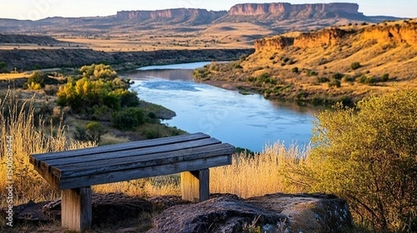 Fototapeta Wooden bench overlooks a serene river valley, with colorful hills in the background