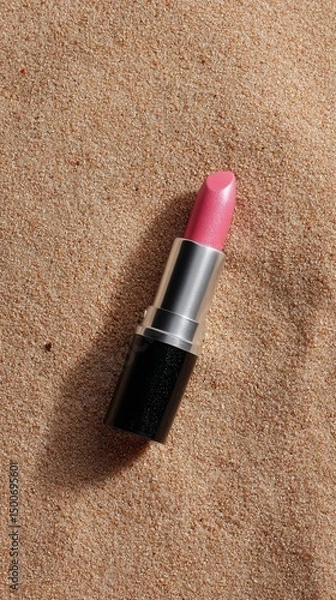 Fototapeta Pink lipstick on beige sand, showcasing a summer beauty concept.  Simple, elegant product presentation against a textured background. Free space for text