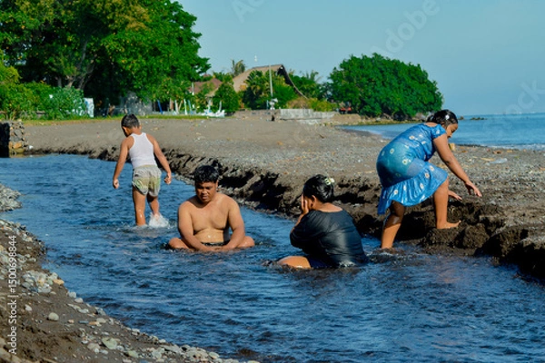 Fototapeta Parents soak in the stream while the daughter walks to shore and the boy explores midstream.