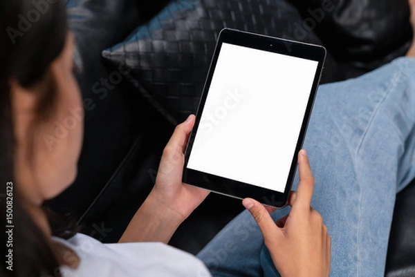 Fototapeta Hand holding digital tablet with blank screen for graphic display montage on the sofa in the living room, mockup display for lifestyle and wireless technology.