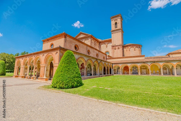 Fototapeta Saint Christopher Church and the large cloister of the Charterhouse of Ferrara, surrounded by cypress trees and a well-kept lawn, stand out against a clear blue sky on a sunny day