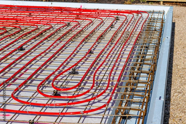 Obraz Underfloor heating system with red pipes on construction site, Close-up of underfloor heating installation using red pipes laid on a foundation grid at a building