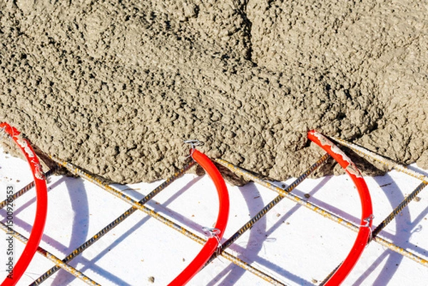 Obraz Concrete pouring over underfloor heating pipes and mesh, Red underfloor heating pipes attached to a steel mesh grid being covered with freshly poured concrete.